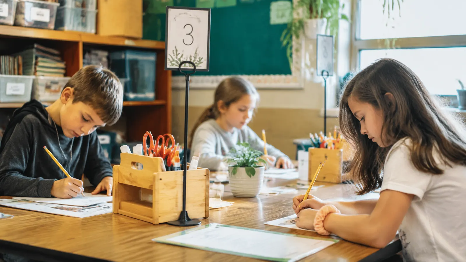 Classroom table group with four GAMENOTE wooden desk organizers at each corner, students working on an art project